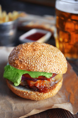 Big tasty hamburger on a paper with light beer in glass mug, close up