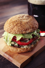 Glass mug of dark beer with hamburger on wooden table, close up