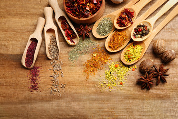 Assorted spices in spoons on wooden table, top view