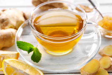 Glass cup of green tea with lemon and ginger root on wooden table closeup