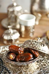 Composition of dried dates in holiday dish and rosary on wooden background closeup