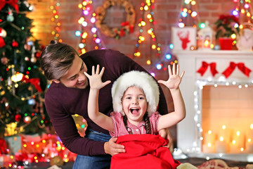 Fototapeta na wymiar Funny little sister in Santa sack surprising her older brother on Christmas background