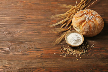 Fresh baked bread, a bowl of flour and wheat ears on the wooden background