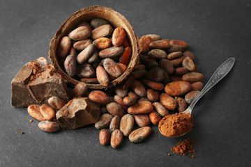 Bowl with aromatic cocoa beans and chocolate on grey background, close up