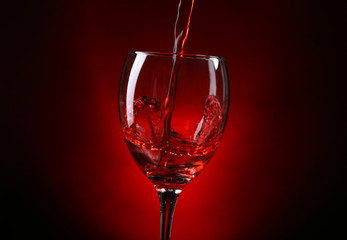 Wine pouring in glass on dark red background