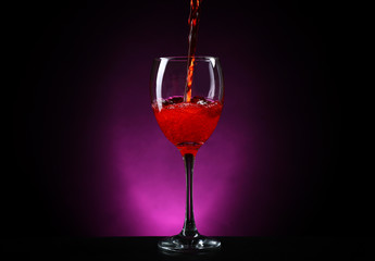 Wine pouring in glass on dark purple background