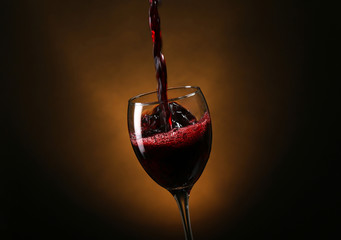 Naklejka na ściany i meble Wine pouring in glass on brown background