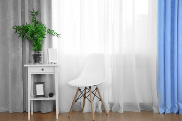Small white table with green plant and chair on curtain background