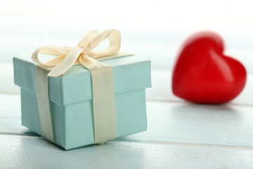 Gift box and decorative hearts on color wooden table, on light background