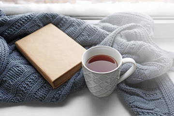 Cup of tea, book and warm knitted plaid on windowsill, close up