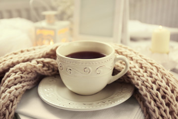 Cup of tea and knitted scarf on coffee table in the room, close up