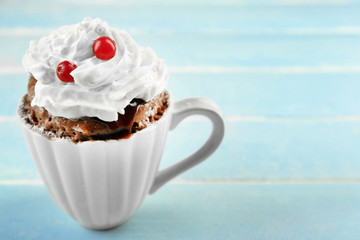 Mug cake with cream and cranberry on blue wooden background