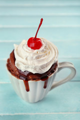 Chocolate mug cake with cream and cherry on blue wooden background