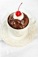 Chocolate mug cake with cream and cherry on a white napkin