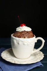 Chocolate mug cake with cream and cherry on a table in front of dark background