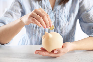 Female hand putting coin into piggy bank closeup