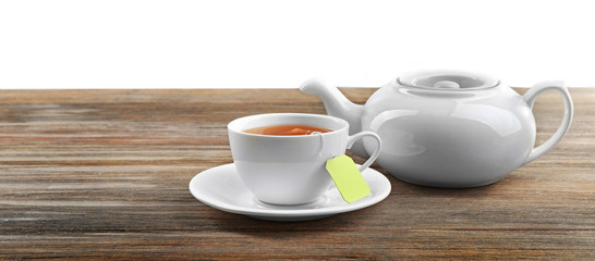 Fototapeta na wymiar Cup of tea with tea bags and teapot on wooden background against grey background
