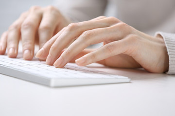 Female hands using keyboard on white wooden table, close up