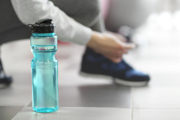Bottle of water and woman tying shoelaces of sneaker on a floor