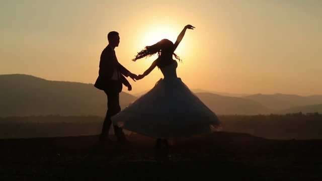 Silhouettes of wedding couple gracefully dances in the mountains