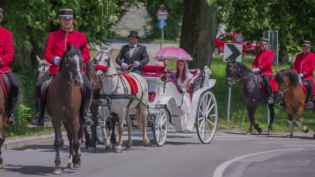 Men in uniforms on horses and a carriage are driving through town