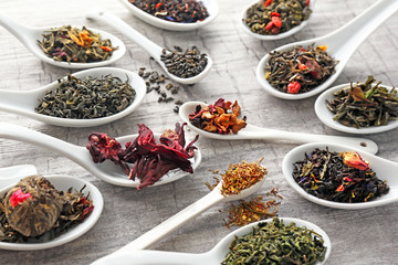 Obraz na płótnie Canvas Variety of dry tea in white spoons on grey wooden background