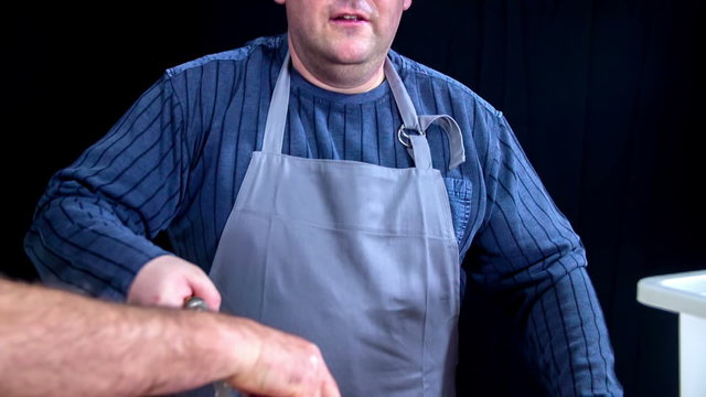 A man pauses for a second and then continues griding meat