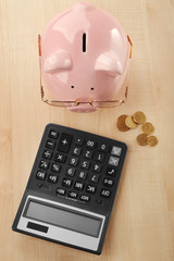 Pink piggy bank with coins, glasses and calculator on light wooden background