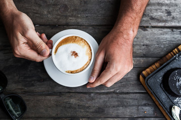 Cappuccino cup in male hands. Vintage style. Top view wooden bla