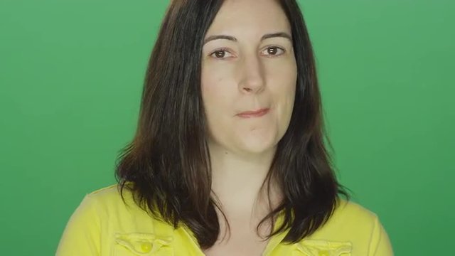 Young brunette woman casually flirts and smiles, on a green screen studio background