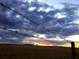 Sunset and cloudy sky behind barb fence