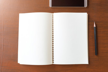Blank note book with pencil and smartphone on wooden table backg