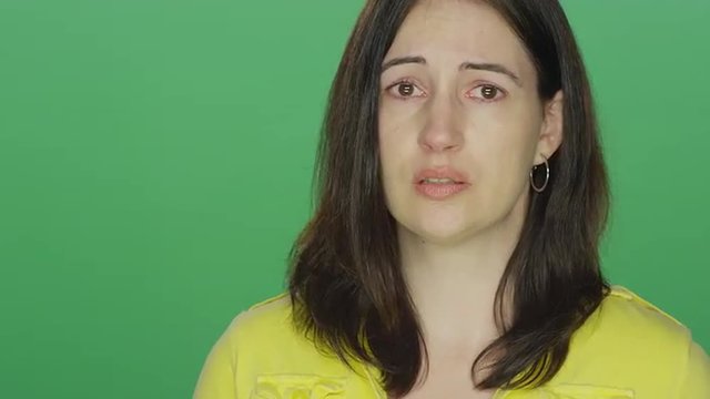 Young brunette woman begins to tear up, on a green screen studio background