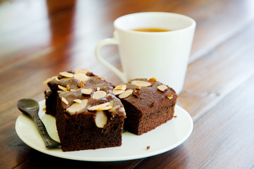 Chocolate brownie on white plate and cup of tea on wooden table