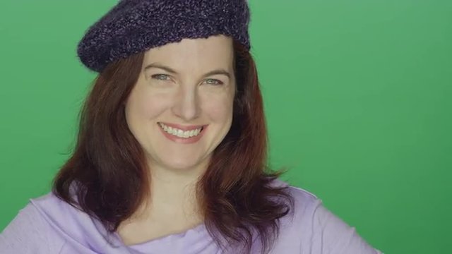 Young redhead woman wearing a beret smiling, on a green screen studio background 