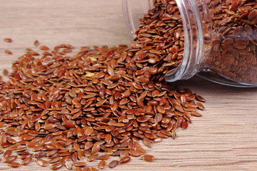Linseed spilling out of jar on wooden background
