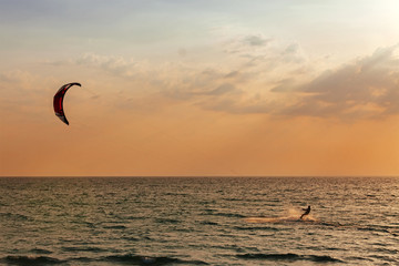 Kite surfer sailing in the sea at sunset