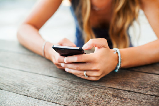 young cute girl hipster, sitting at a cafe holding a smart phone, answering texts, phone calls, letters, posts photos in instagram, outdoor portrait, close up, elaborated and bracelets on the hands