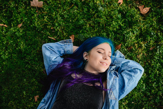 Teenage woman with blue hair lying on the grass