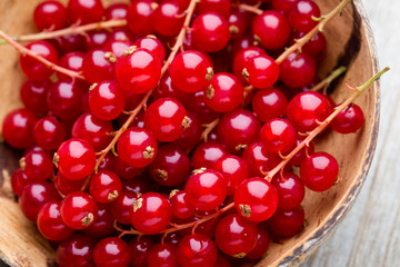 Redcurrant on a branch close to a wooden bowl.