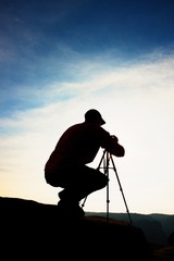 Professional photographer takes photos with camera on tripod on rocky peak. Dreamy spring landscape.