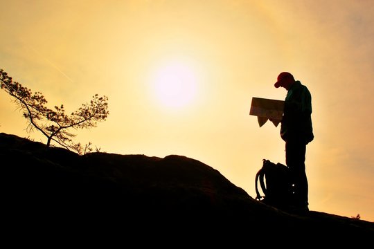 Silhouette of young man looking at a map in nature while hiking