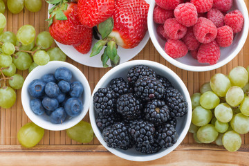 fresh berries in a bowl and green grapes on wooden tray