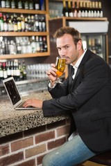 Handsome man using laptop computer and drinking a beer