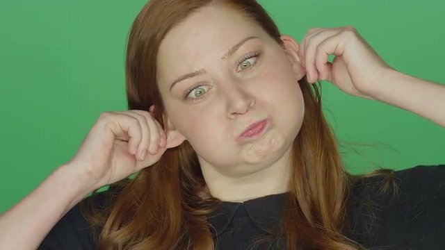 Young redhead woman smiling and making silly faces, on a green screen studio background