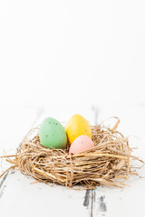 tre pastellfärgade ägg i ett fågelbo på vit trä bakgrund