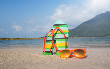 Holiday.sand on the beach,flip flops and sunglasses with sea and mountains on background