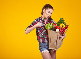 Smiling woman carrying a bag with vegetables. Yellow background.