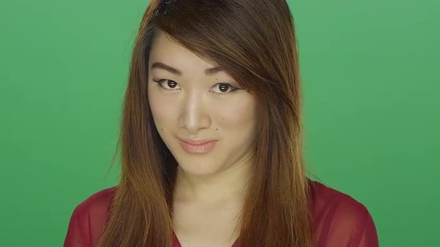 Young Asian woman shyly staring, on a green screen studio background 