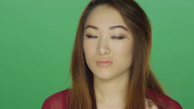 Young Asian woman awkwardly staring, on a green screen studio background 